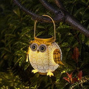 May include: A yellow metal owl-shaped solar lantern featuring a perforated body that emits a warm glow. The lantern has large circular eyes, two wings, and a handle for hanging. The design includes intricate cutouts that create a light pattern.