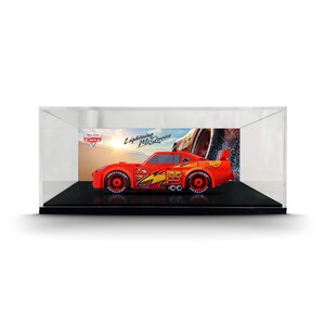 May include: A red Lightning McQueen toy car constructed from building blocks, featuring the number 95, yellow lightning bolt graphics, and black wheels, displayed inside a clear rectangular acrylic case with a Cars themed backdrop.