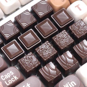 Pode incluir: Um conjunto de teclas para teclado mecânico em tons de castanho chocolate. Algumas teclas têm superfícies quadradas lisas, enquanto outras apresentam texturas rugosas ou padrões de linhas onduladas. A tecla Caps Lock está visível.