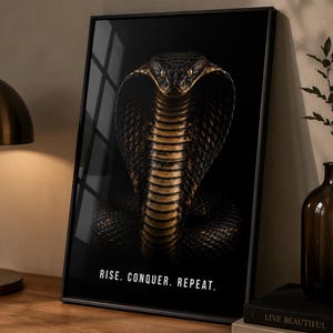 Puede incluir: Una impresión de arte mural vertical enmarcada que presenta una ilustración detallada de una cobra con escamas negras y doradas sobre un fondo oscuro. El texto "RISE. CONQUER. REPEAT." está impreso en letras mayúsculas blancas en la parte inferior.