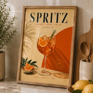 Puede incluir: Una lámina enmarcada que muestra una copa de spritz naranja con hielo y una ramita de romero. El texto dice SPRITZ, VIBRANT FRESH ITALIAN, La dolce vita y ORANGE PROSECCO SODA. Un pequeño cuenco con rodajas de naranja acompaña a la copa.