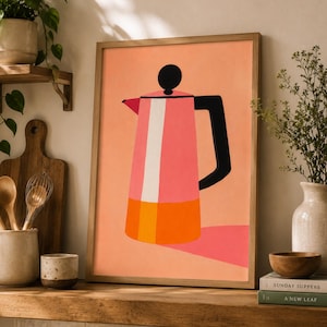May include: A framed wall art print featuring a stylized illustration of a moka pot. The coffee maker is depicted with a pink upper body, an orange base, and a black handle and lid knob, set against a solid peach-colored background.