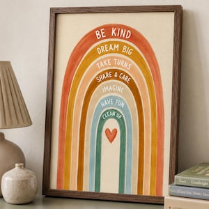 May include: A framed wall art print featuring a multi-coloured rainbow with the text BE KIND, DREAM BIG, TAKE TURNS, SHARE & CARE, IMAGINE, HAVE FUN, CLEAN UP, and a small red heart. The rainbow has bands of orange, yellow, tan, and blue.
