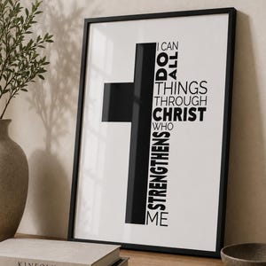 May include: A framed vertical wall art print featuring a bold black cross shape against a white background. The text I CAN DO ALL THINGS THROUGH CHRIST WHO STRENGTHENS ME is printed in black sans-serif font, integrated into the cross design.