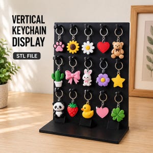 May include: A black vertical keychain display stand with fifteen hooks holding various colourful keychains, including a bear, panda, duck, strawberry, cactus, and flowers. The text VERTICAL KEYCHAIN DISPLAY STL FILE is printed on the left side.