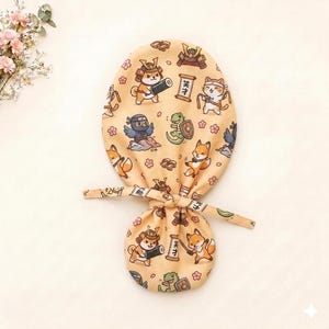 Può includere: Una cuffia in tessuto beige con un motivo ripetuto di animali dei cartoni animati vestiti da samurai e ninja, tra cui volpi, un cane e una lucertola, intervallati da fiori di ciliegio e pergamene con caratteri giapponesi per talento.