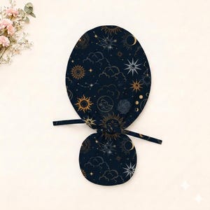 May include: A dark navy blue scrub cap featuring a celestial pattern of gold and white suns, moons, stars, and clouds. The cap has a rounded top section and a smaller circular back panel, with two fabric ties extending from the sides for adjustment.
