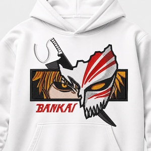 Op de afbeelding: Een witte hoodie met een geborduurde afbeelding van een personage met stekelig oranje haar en een wit masker met rode strepen. Het ontwerp bevat een zwart rechthoekig kader, een zwaard en de rode tekst BANKAI die eronder is gedrukt.