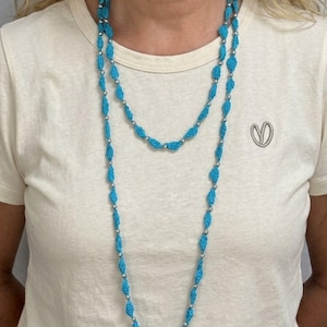Puede incluir: Un collar largo que presenta un patrón repetitivo de cuentas de ganchillo en color turquesa brillante y pequeñas esferas metálicas pulidas en tono plateado. El collar está diseñado como una hebra continua que puede llevarse doble.