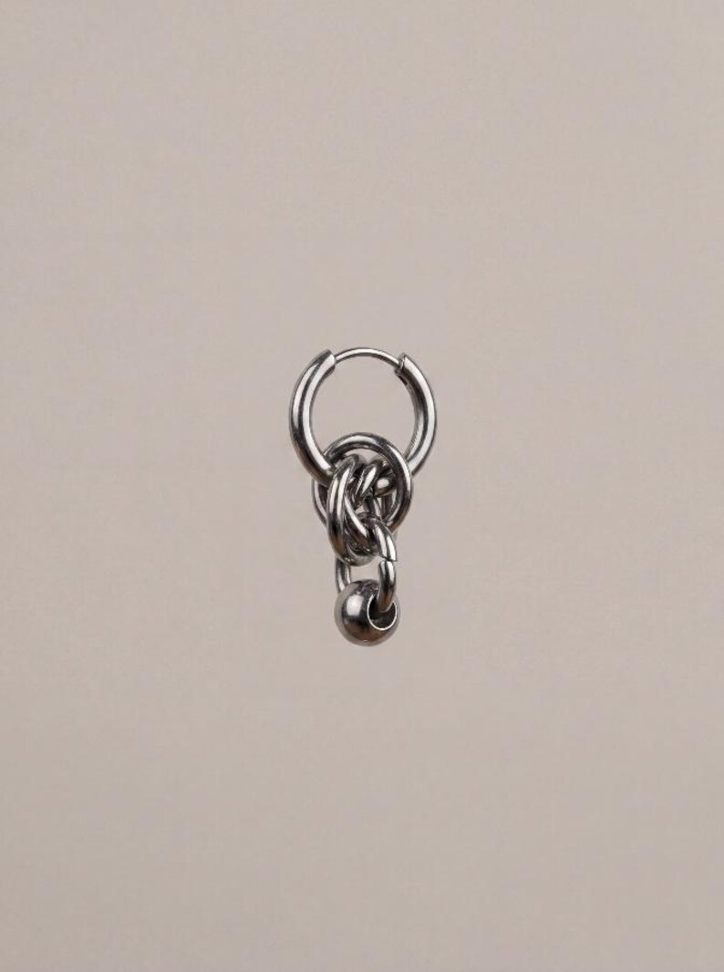 May include: A silver-toned hoop earring featuring a dangling charm composed of two interlocking metal rings and a single small, smooth spherical bead at the base. The earring has a polished metallic finish and a hinged closure mechanism.