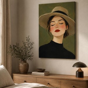May include: A canvas wall art print featuring a portrait of a person wearing a wide-brimmed beige hat with a black band and a black high-neck top. The subject has closed eyes, rosy cheeks, and bright red lips, set against a solid olive green background.