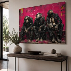 Puede incluir: Un gran cuadro rectangular de pared que muestra a tres chimpanc&eacute;s vestidos con trajes oscuros y corbatas, sentados uno al lado del otro sobre un fondo vibrante de color magenta y rosa con salpicaduras de pintura y texturas.