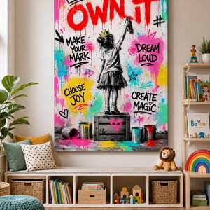 May include: A vertical wall art print featuring a black and white illustration of a child wearing a crown and standing on a crate, spray painting the text OWN IT in red. The background is filled with colorful paint splatters and phrases.