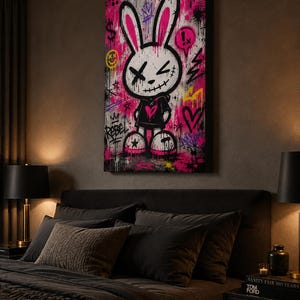 May include: A rectangular canvas wall art piece featuring a graffiti-style illustration of a white rabbit character with long ears, X-shaped eyes, and a stitched mouth. The rabbit wears a black hoodie with a pink heart and stands against a vibrant pink and black background filled with spray paint splatters, crowns, dollar signs, and the word REBEL.