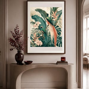 Puede incluir: Una l&aacute;mina de arte enmarcada que muestra dos aves quetzal posadas entre un exuberante follaje tropical, grandes hojas de palmera verdes y flores de color rosa p&aacute;lido. La obra est&aacute; en un marco marr&oacute;n oscuro sobre una mesa consola beige.