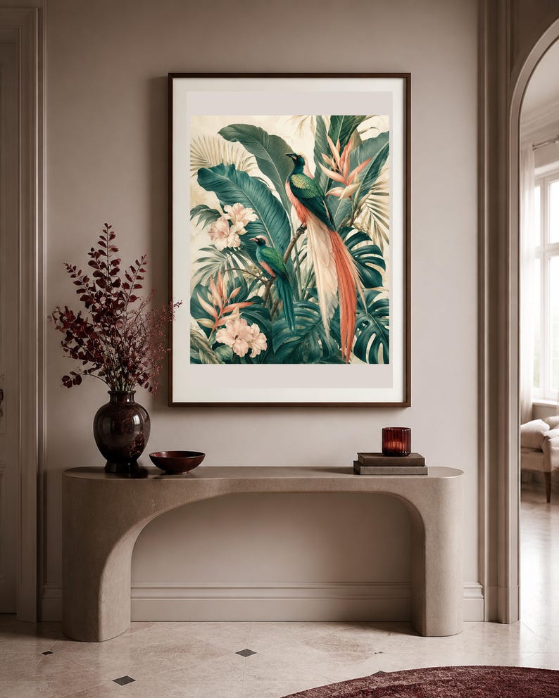 Puede incluir: Una l&aacute;mina de arte enmarcada que muestra dos aves quetzal posadas entre un exuberante follaje tropical, grandes hojas de palmera verdes y flores de color rosa p&aacute;lido. La obra est&aacute; en un marco marr&oacute;n oscuro sobre una mesa consola beige.