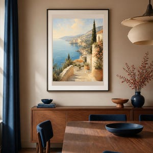 Puede incluir: Una impresi&oacute;n art&iacute;stica enmarcada que representa un paisaje costero mediterr&aacute;neo con una escalera de piedra que conduce hacia un mar azul, edificios con techos de terracota, cipreses y plantas en macetas bajo un cielo soleado.