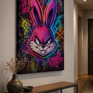 Peut inclure: Une impression d'art mural rectangulaire repr&eacute;sentant une t&ecirc;te de lapin rose stylis&eacute;e aux contours n&eacute;on avec une expression agressive. Le fond est un collage de style graffiti sombre et textur&eacute; avec des &eacute;claboussures de peinture bleue, jaune et rose, incluant le texte "NO RULES" et "REBEL" en lettres peintes &agrave; la bombe.