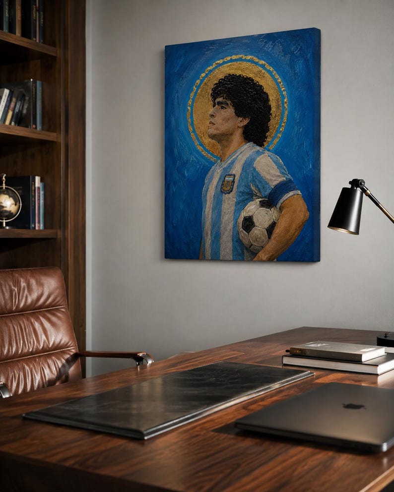 May include: A rectangular canvas painting depicting a man with dark curly hair wearing a light blue and white striped jersey, holding a soccer ball. A gold circular halo surrounds the head against a textured blue background, creating a portrait.
