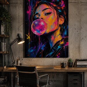 Puede incluir: Una vibrante impresi&oacute;n de arte mural que presenta un retrato estilizado de una persona soplando una gran burbuja de chicle de color rosa brillante. La obra utiliza un fondo oscuro con salpicaduras energ&eacute;ticas de pintura azul ne&oacute;n, amarilla y magenta.