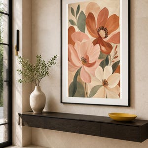 Puede incluir: Una impresi&oacute;n de arte mural vertical enmarcada que presenta una ilustraci&oacute;n bot&aacute;nica de flores grandes en tonos terracota, rosa suave y crema, acentuadas por hojas de color verde apagado, en un marco negro fino sobre una pared neutra.