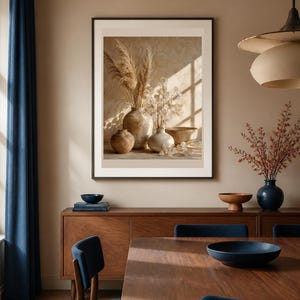 K&ouml;nnte beinhalten: Ein gerahmter Wandkunstdruck mit einem Stillleben aus drei Keramikvasen und einer Schale, gef&uuml;llt mit getrocknetem Pampasgras und zarten Blumen, beleuchtet durch weiches Sonnenlicht, das Fensterkreuzschatten auf den beigen Hintergrund wirft.