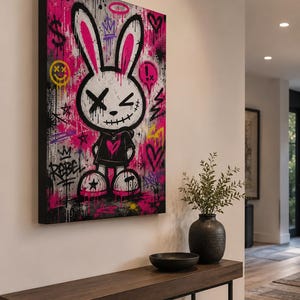 May include: A rectangular canvas wall art piece featuring a stylized cartoon rabbit with long pink-lined ears, X-shaped eyes, and a stitched mouth. The background is a vibrant mix of hot pink, black, and white graffiti with symbols like hearts, stars, and the word REBEL.