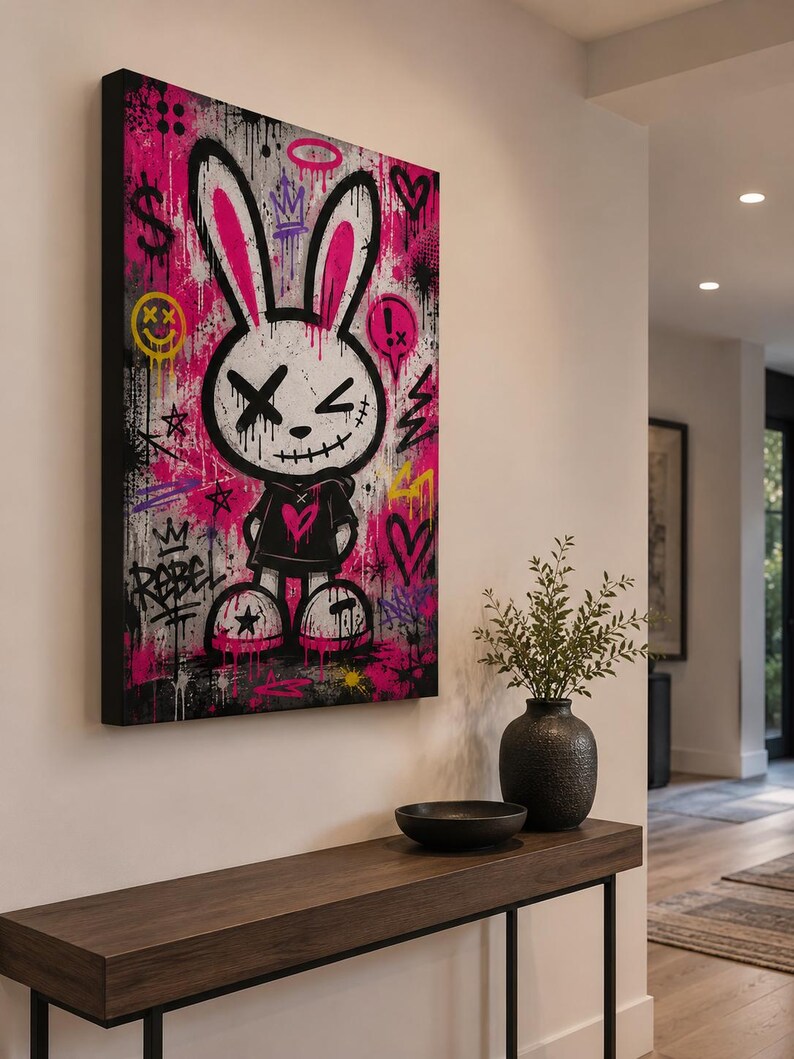 May include: A rectangular canvas wall art piece featuring a stylized cartoon rabbit with long pink-lined ears, X-shaped eyes, and a stitched mouth. The background is a vibrant mix of hot pink, black, and white graffiti with symbols like hearts, stars, and the word REBEL.
