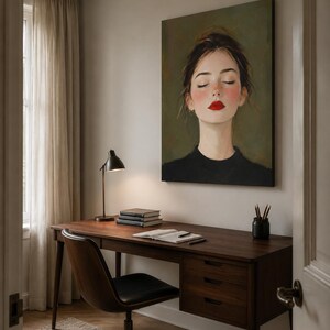 Puede incluir: Una gran impresi&oacute;n de arte mural rectangular que muestra el retrato de una persona con los ojos cerrados, mejillas sonrosadas y labios rojos brillantes, vistiendo una prenda negra sobre un fondo verde oliva, colgada sobre un escritorio de madera.