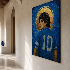 May include: A rectangular canvas painting featuring a portrait of a footballer with dark curly hair, wearing a blue jersey with the number 10 in white. The figure is set against a deep blue background with a prominent gold circular halo behind the head.