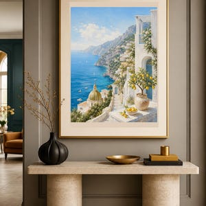 May include: A framed wall art print depicting a coastal Mediterranean scene with a blue sea, a golden domed church, white buildings, and a potted lemon tree. The artwork is displayed in a thin gold frame with a wide cream-colored matting border.