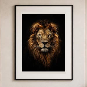 May include: A framed wall art print featuring a high-contrast portrait of a lion with a thick, golden-brown mane against a solid black background. The artwork is encased in a thin black frame with a wide white mat border, centered on the wall.