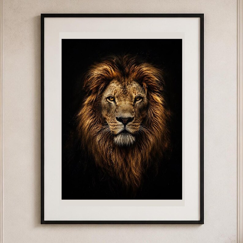 May include: A framed wall art print featuring a high-contrast portrait of a lion with a thick, golden-brown mane against a solid black background. The artwork is encased in a thin black frame with a wide white mat border, centered on the wall.