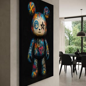 Op de afbeelding: Een rechthoekig wandkunstwerk met een gestileerde berenfiguur tegen een effen zwarte achtergrond. De beer is bedekt met levendige graffiti-achtige verfspatten, waaronder blauw, oranje en roze, met handgetekende symbolen zoals een ster en hart.