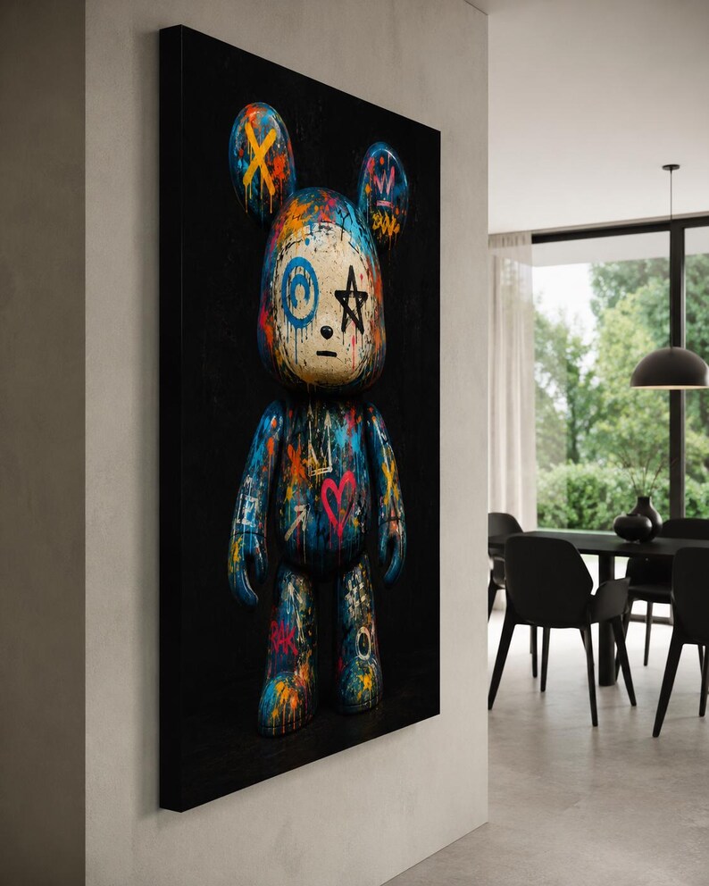 Op de afbeelding: Een rechthoekig wandkunstwerk met een gestileerde berenfiguur tegen een effen zwarte achtergrond. De beer is bedekt met levendige graffiti-achtige verfspatten, waaronder blauw, oranje en roze, met handgetekende symbolen zoals een ster en hart.