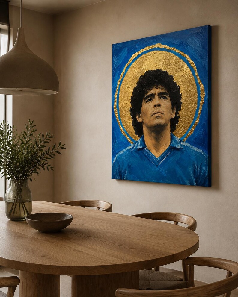 Puede incluir: Un cuadro rectangular sobre lienzo que muestra el retrato de un hombre de pelo oscuro y rizado con una camisa de cuello azul. La figura est&aacute; centrada sobre un fondo azul vibrante con un gran halo circular de pan de oro texturizado detr&aacute;s.