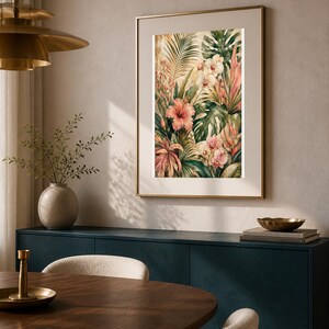 May include: A framed wall art print featuring a botanical illustration of tropical foliage, including large green monstera leaves, pink hibiscus flowers, and white orchids, set against a warm, muted background with golden highlights.
