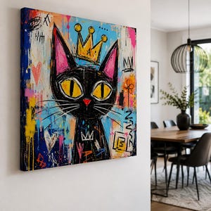 Pode incluir: Uma tela quadrada apresentando um gato preto estilizado com grandes olhos amarelos e um pequeno nariz vermelho. O gato usa uma coroa amarela. O fundo &eacute; uma mistura vibrante de respingos de tinta azul, rosa e amarela com marcas de graffiti.