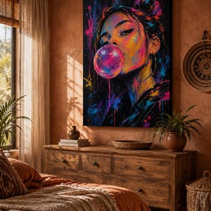 Puede incluir: Un lienzo rectangular para pared que presenta un retrato abstracto y vibrante de una persona soplando una gran burbuja de chicle de color rosa brillante. La obra utiliza salpicaduras audaces de pintura azul ne&oacute;n, amarilla y magenta.