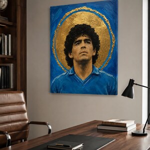Puede incluir: Un cuadro rectangular sobre lienzo que muestra el retrato de un hombre de pelo oscuro y rizado con una camisa azul de cuello. La figura se sit&uacute;a sobre un fondo azul intenso con un gran halo circular de pan de oro con textura.