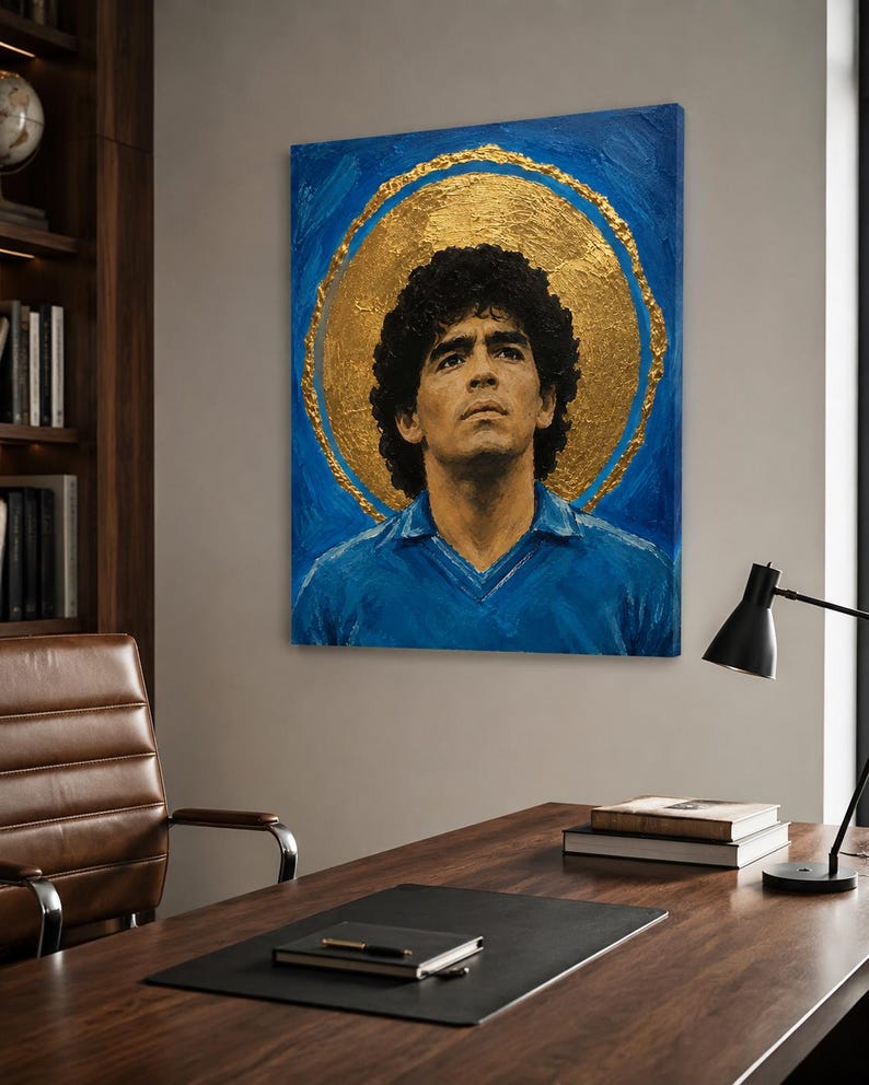 Puede incluir: Un cuadro rectangular sobre lienzo que muestra el retrato de un hombre de pelo oscuro y rizado con una camisa azul de cuello. La figura se sit&uacute;a sobre un fondo azul intenso con un gran halo circular de pan de oro con textura.