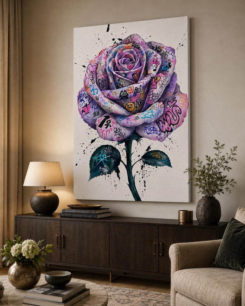 Puede incluir: Un cuadro rectangular sobre lienzo que presenta una gran rosa morada central cubierta de coloridos grafitis, s&iacute;mbolos y texto. La rosa tiene un tallo verde con dos hojas, todo ello acentuado por salpicaduras de pintura negra sobre un fondo blanco.