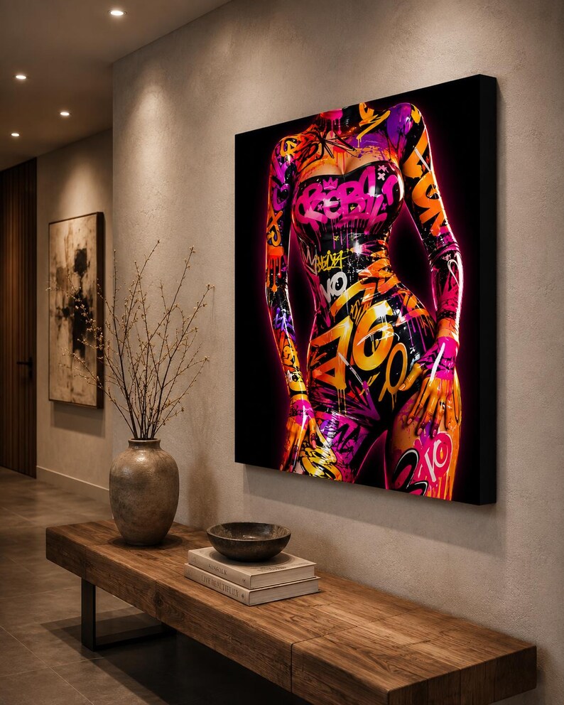 Puede incluir: Un lienzo rectangular para pared que presenta una vibrante ilustraci&oacute;n estilo grafiti de un torso. La obra muestra patrones de pintura en aerosol rosa ne&oacute;n, naranja y morado, incluyendo la palabra REBEL, sobre un fondo negro profundo.