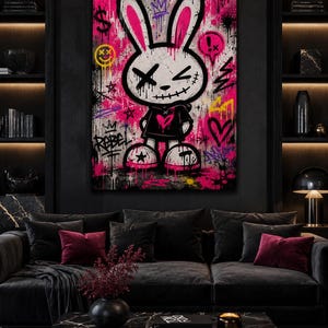 May include: A rectangular wall art piece featuring a stylized cartoon rabbit with X-shaped eyes and a stitched mouth. The character wears a black hoodie with a pink heart, set against a vibrant pink and black graffiti-style background with symbols.