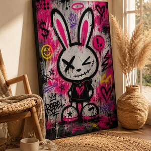 May include: A rectangular canvas wall art piece featuring a stylized white rabbit character with black outlines, X-shaped eyes, and a stitched mouth. The background is a vibrant mix of hot pink, black, and white graffiti with symbols like hearts, stars, and the word REBEL.