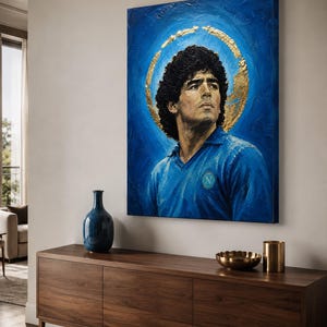 Puede incluir: Un cuadro rectangular sobre lienzo que muestra el retrato de un hombre de pelo oscuro y rizado con una camisa azul de cuello con un logotipo circular en el pecho. Un halo dorado texturizado rodea la cabeza sobre un fondo azul intenso.