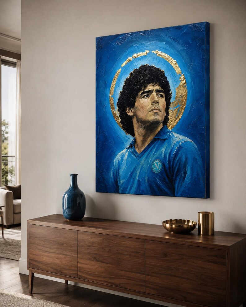 Puede incluir: Un cuadro rectangular sobre lienzo que muestra el retrato de un hombre de pelo oscuro y rizado con una camisa azul de cuello con un logotipo circular en el pecho. Un halo dorado texturizado rodea la cabeza sobre un fondo azul intenso.