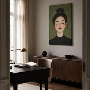 Puede incluir: Un cuadro rectangular sobre lienzo que muestra el retrato de una persona con el cabello oscuro recogido en un mo&ntilde;o alto, ojos cerrados y labios de color rojo brillante, sobre un fondo verde oliva s&oacute;lido, expuesto en una oficina en casa.