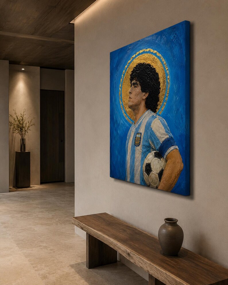 May include: A square canvas painting featuring a portrait of a soccer player with dark curly hair, wearing a light blue and white striped jersey with an emblem, holding a soccer ball, set against a vibrant blue background with a gold halo.