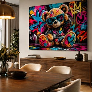 May include: A rectangular wall art canvas featuring a brown teddy bear wearing a black jacket and bright blue sunglasses. The background is a vibrant graffiti mural with neon pink, blue, and yellow paint splatters, crowns, and heart symbols.